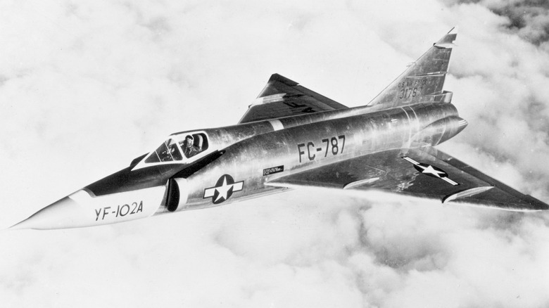 An F-102A Delta Dagger flying over cloudy skies in the 1950s