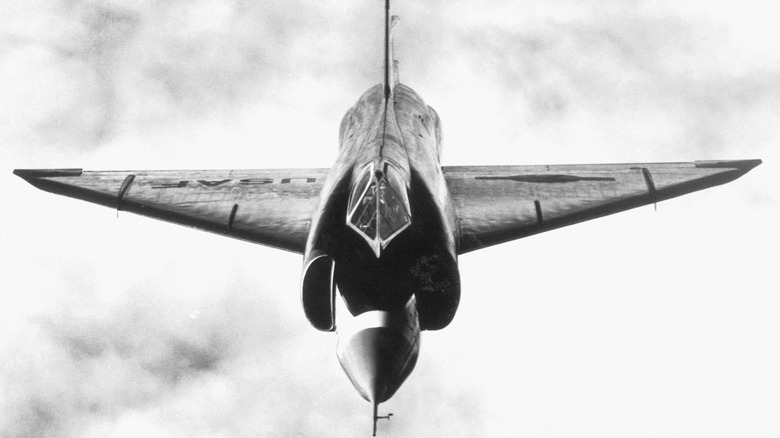 An F-102A Delta Dagger as seen from the front, flying over cloudy skies