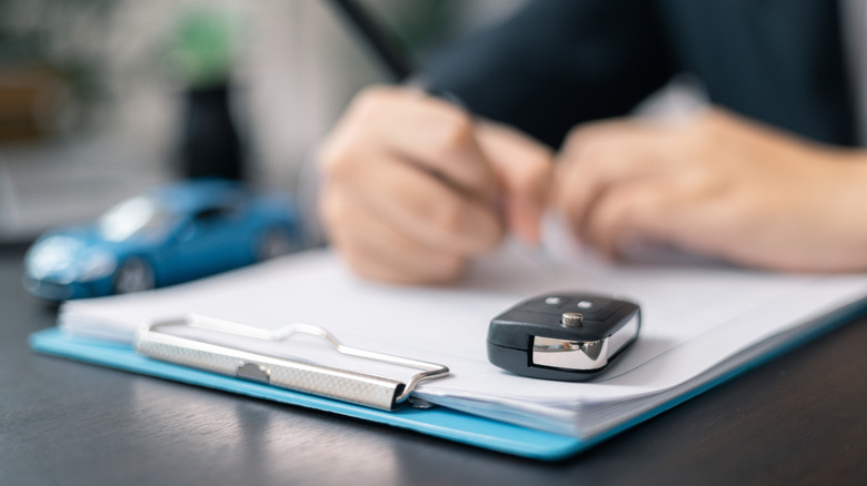 A person filling out car dealership paperwork with a keyfob and a blue model car next to the clipboard