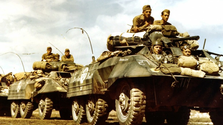 soldiers in an M8 Greyhound driving along a dirt road