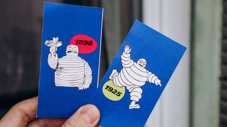 man holds two cards with past versions of the Michelin Man