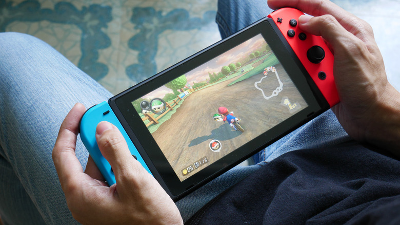 A person holds a Nintendo Switch and plays Mario Kart