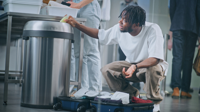 Man Removes Liquids from Suitcase, Throws in Trash Can.