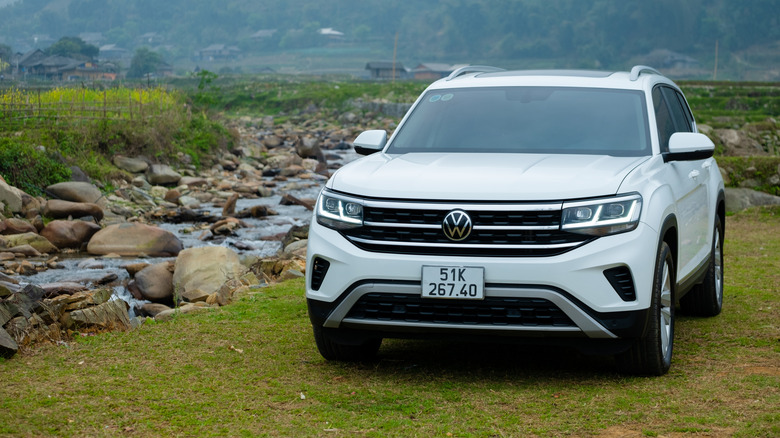 A white Volkswagen Teramont parked near a stream on green grass.