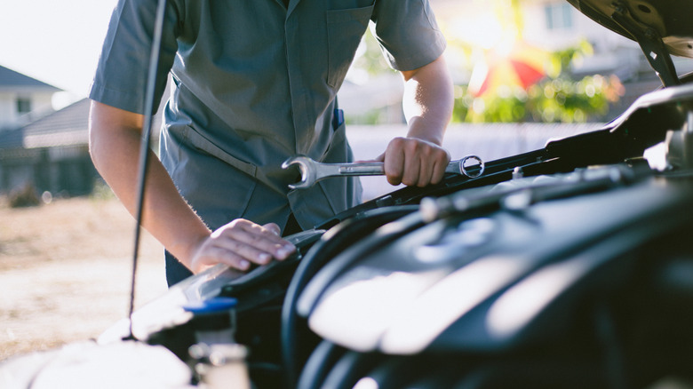 A man holds a wrench while standing in front of an open engine bay.