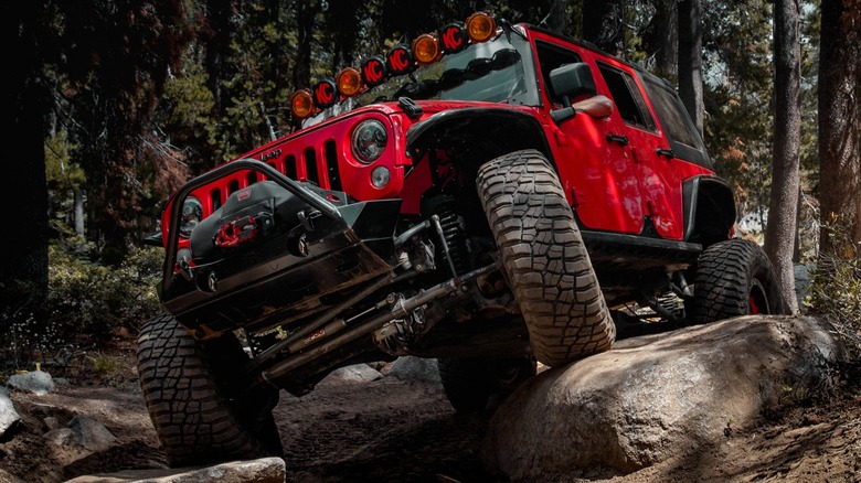 A red Jeep Wrangler negotiating a rugged off-road trail.