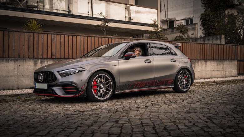 A gray Mercedes-AMG A 45 parked on a cobble street, front 3/4 view, red accents and AMG graphics