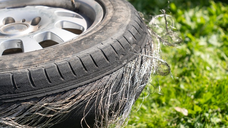 Damaged tire on a grassy ground with steel wires protruding out from it
