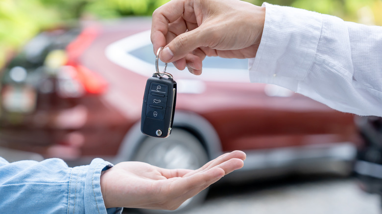 Person hands vehicle keys to another.