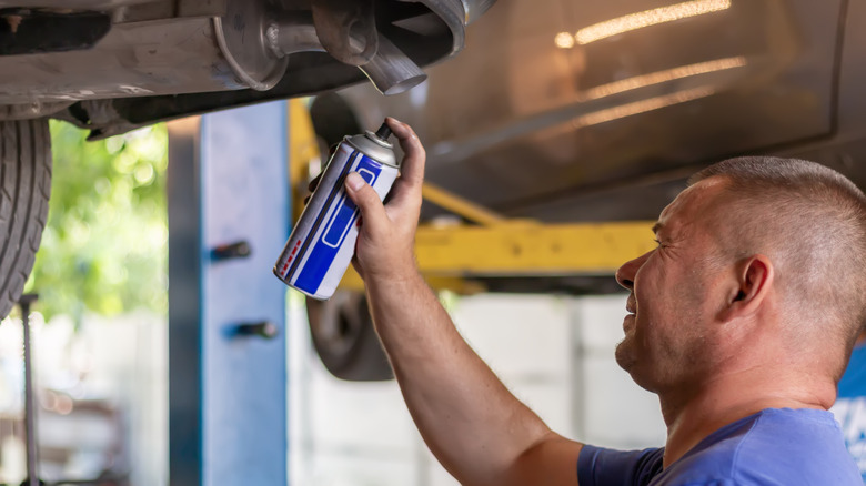 Mechanic spraying anti-corrosion spray on the bottom of a vehicle