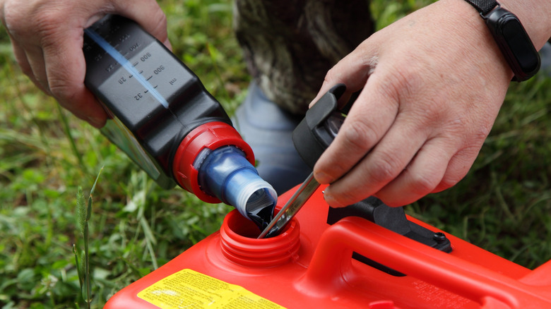 Close up of hands pouring oil into a red plastic container for fuel..