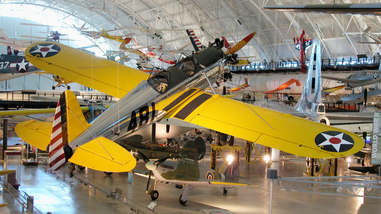 A yellow-winged silver fighter plane suspended from the ceiling in a museum