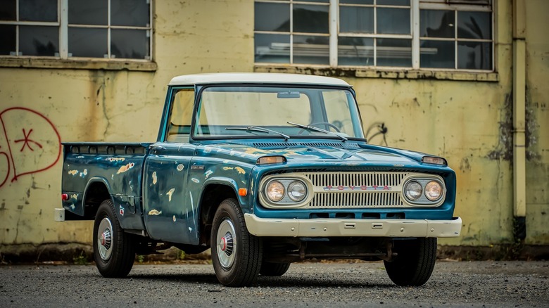 A blue Toyota Stout with some paint imperfections parked in front of an old building, front 3/4 view