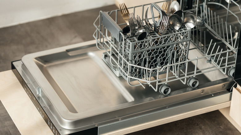 And open dishwasher door without a window showing a basket full of forks.