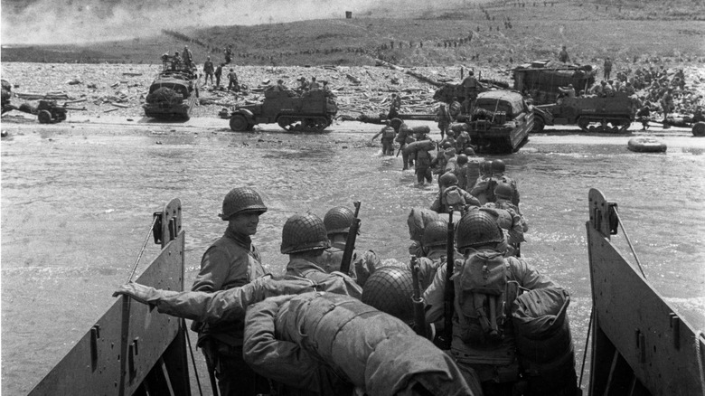 U.S. troops wade ashore from a LCVP landing craft, off "Omaha" Beach, 6 June 1944. Note DUKWs and half-tracks at the water line, lines of men headed inland, and M1903 and M1 rifles carried by some of the troops leaving the landing craft wearing M1 helmets.