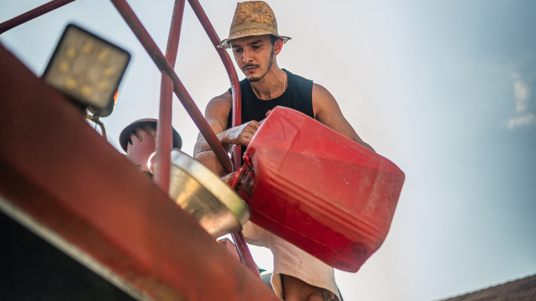 A man fueling a tractor with gasoline during the summer