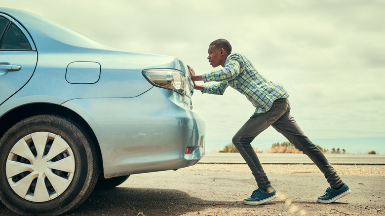 A person pushing a silver car from behind