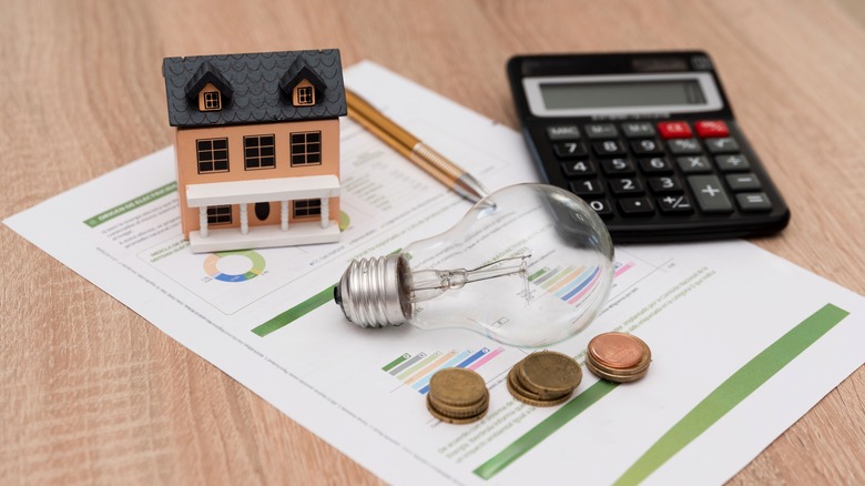 Electricity bill on table with calculator, lightbulb, stacks of pennies, and a model house sitting on top