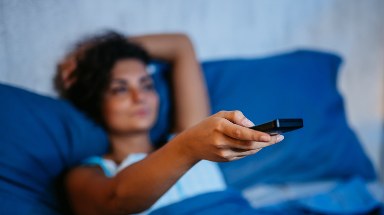 Woman in bed holding TV remote