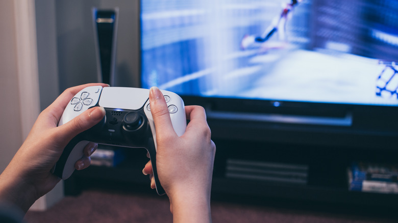 woman holding PlayStation 5 controller in front of TV