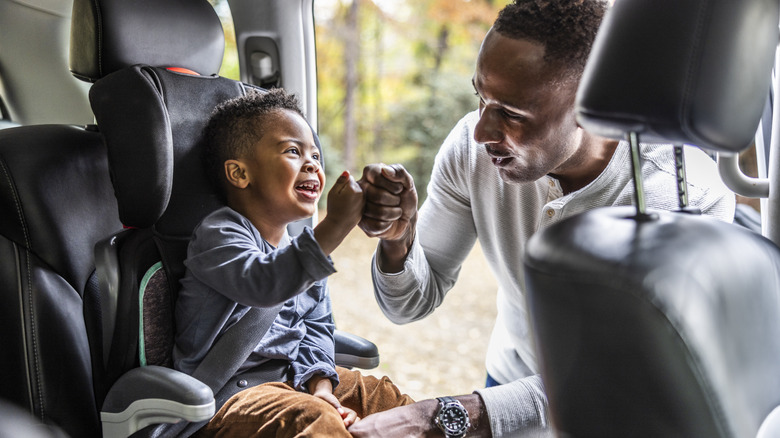 A Dad Getting His Child Settled In The Car Seat And Giving Each Other A Fist Bump