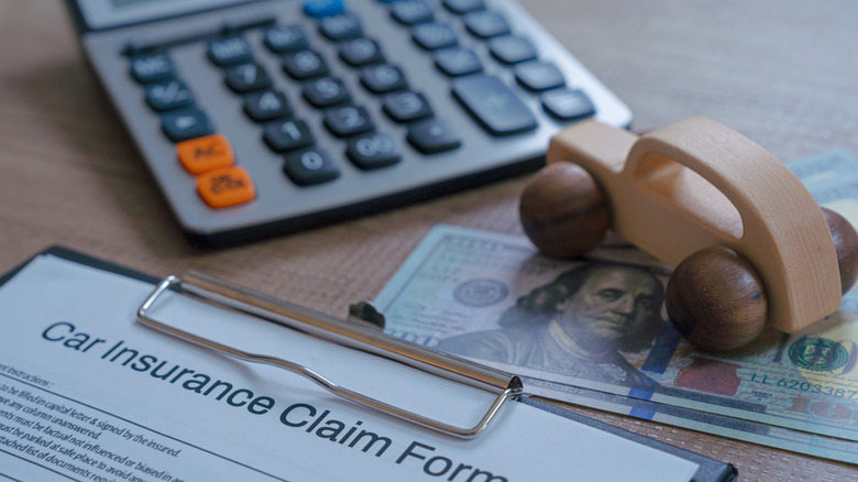 Generic car insurance claim form with calculator, dollar bills, and wooden model car in background