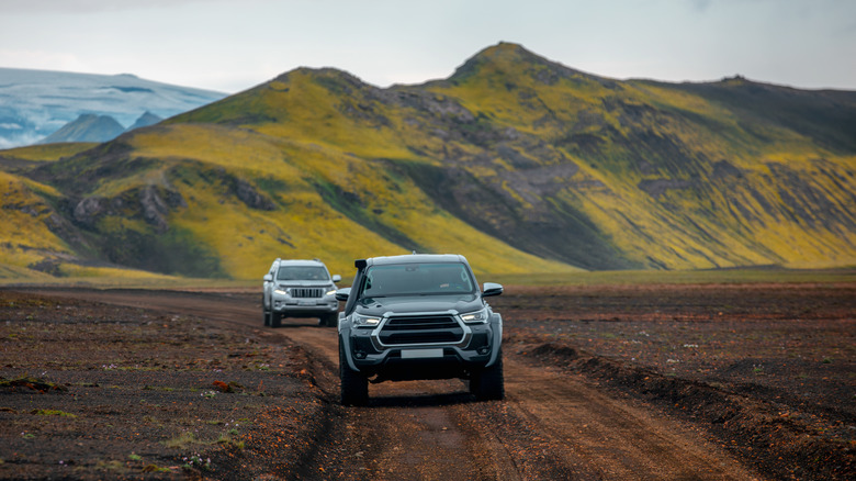 Two Toyota vehicles driving on a dirt road, with a mountain in the background