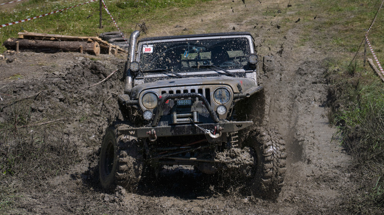 A modified Jeep Wrangler plowing through some mud, front view