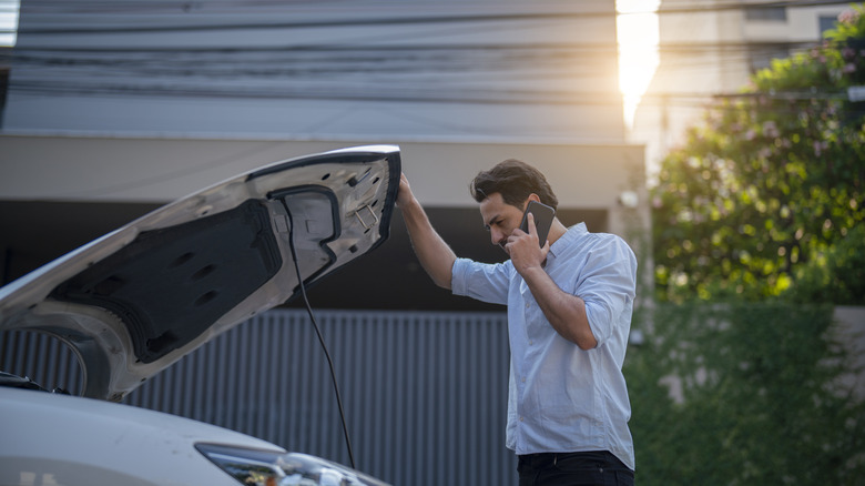 Man on phone looking at broken down car