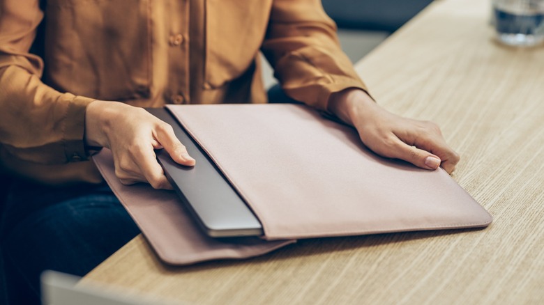 A person placing a laptop in a leather sleeve