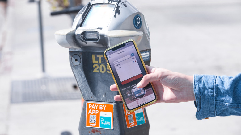person holding an iPhone 11 Pro Max smartphone in front of an LADOT parking meter to pay for a spot