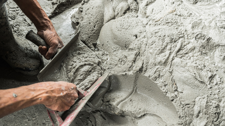 Two hands scoop wet concrete with shovels