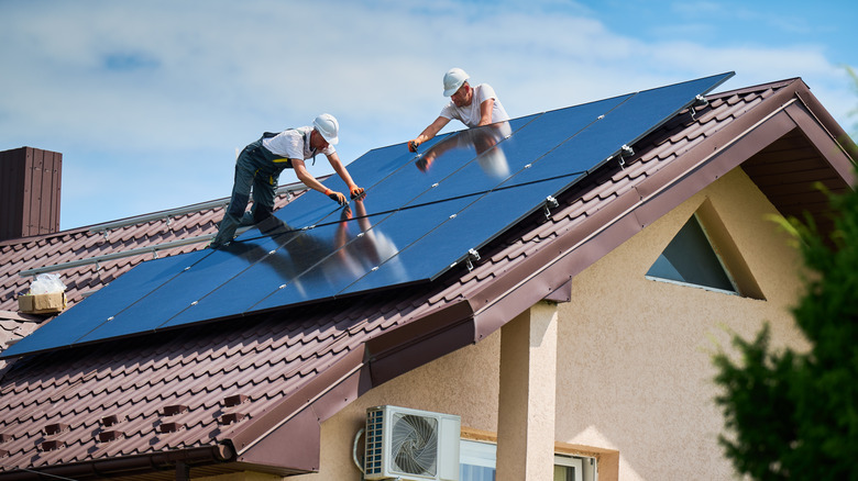 Workers building photovoltaic solar panel system on rooftop of house