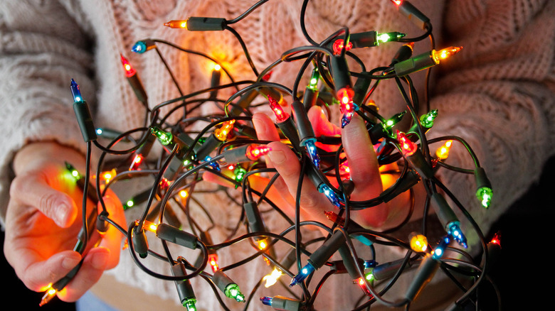 A man holding tangled strands of lit Christmas lights
