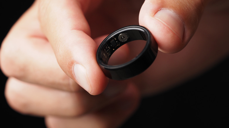 A person holds a smart ring between their thumb and finger.