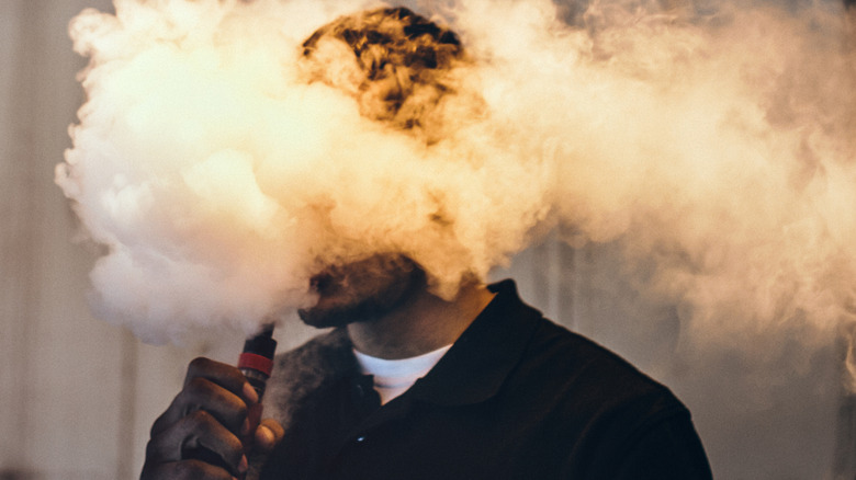Young man covered in cloud of vape smoke