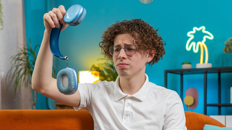 Disappointed young person looking at a damaged wireless headphone
