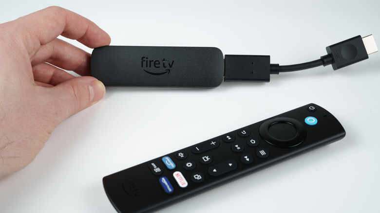 Hand holding Amazon Fire TV connected to HDMI extender with remote