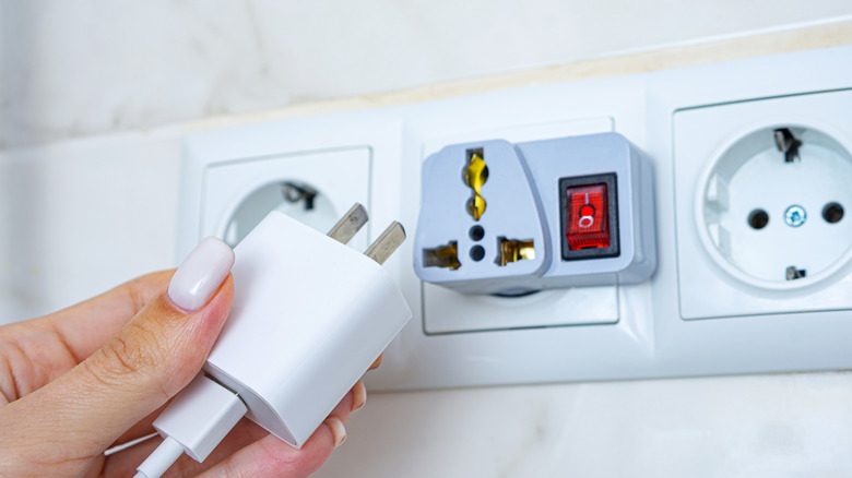 Person preparing to plug American charger plug into an adapter on a European outlet