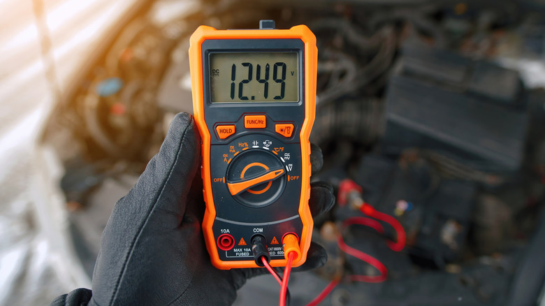 A person holding a multimeter in front of a car.