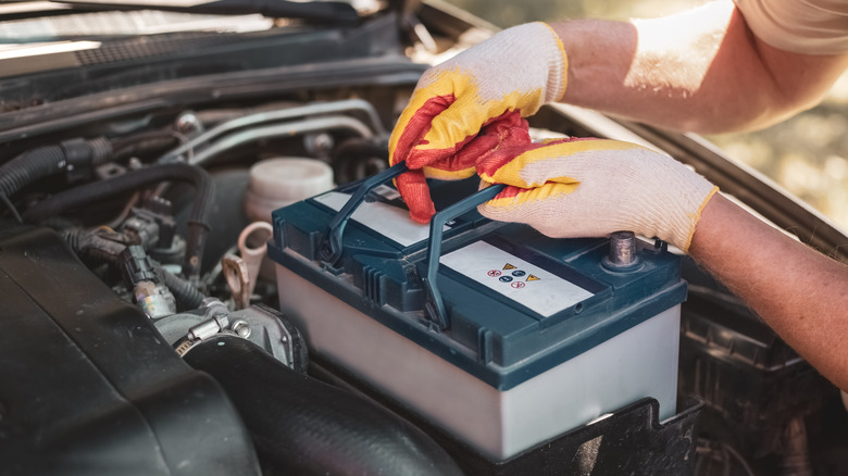 A person putting in a car battery.