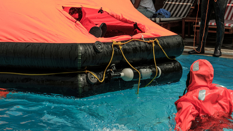 A life raft in the water and a person in a diving suit approaching it