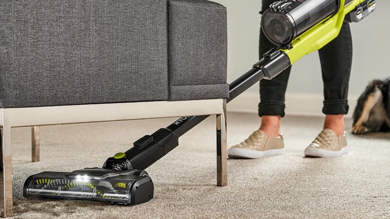 A person using a Ryobi vacuum under a chair.