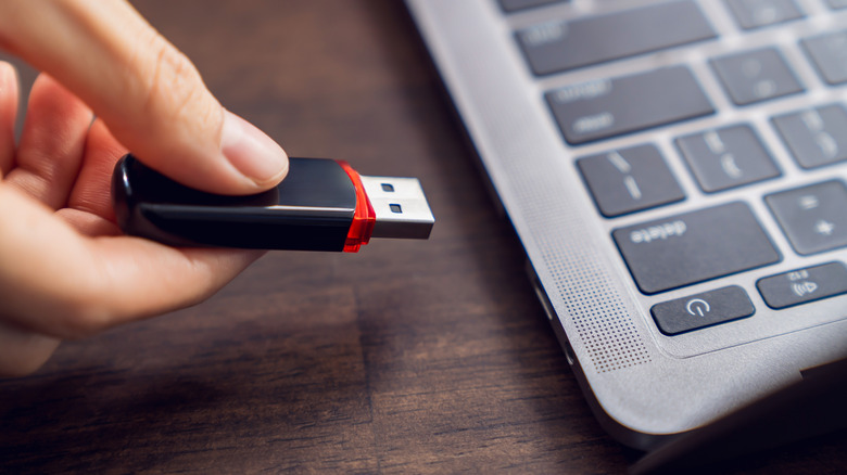 A hand holding a flash drive about to plug it into a laptop