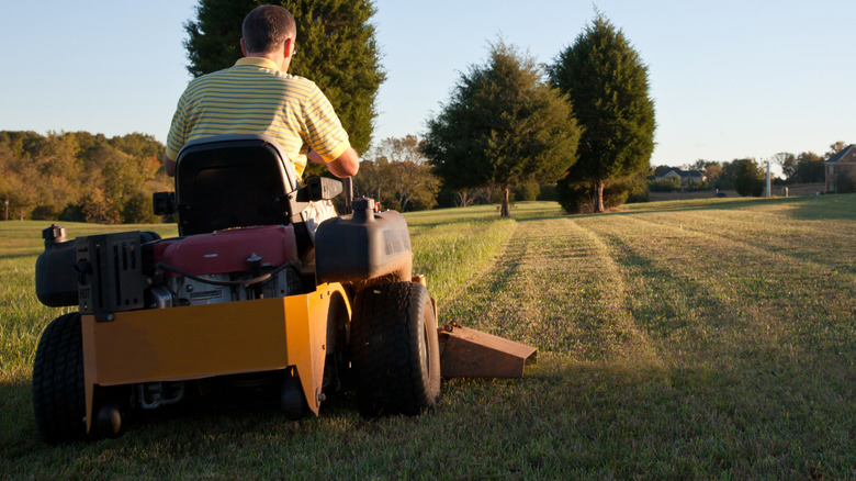 A man on a zero turn mower cutting grass on a sunny day