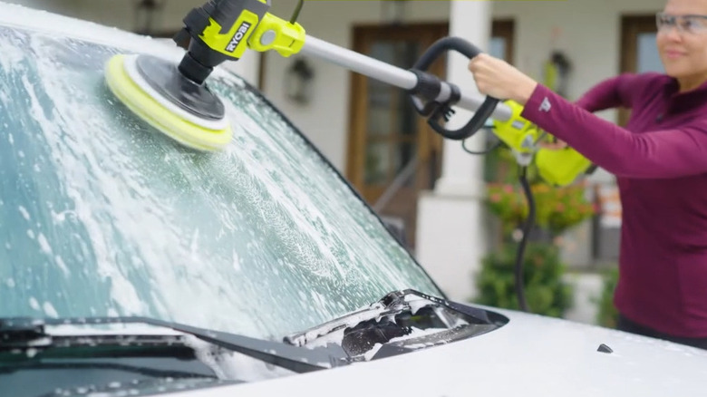 Woman using Ryobi Soap Dispensing Scrubber on car windshield
