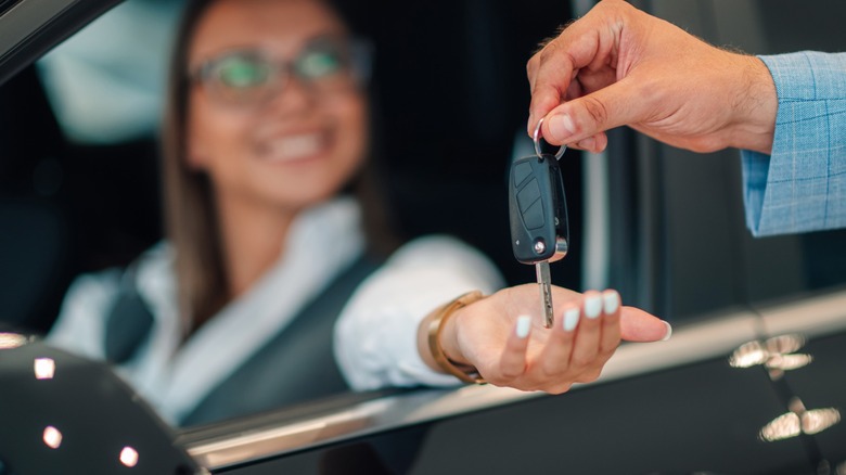 A woman with a smile and an outstretched hand receives car keys