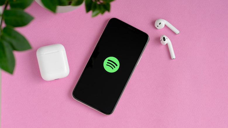 Apple AirPods placed alongside an iPhone with a Spotify logo on screen