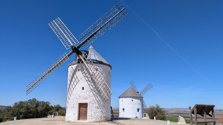 Two traditional white stone windmills with wooden lattice sails standing on a hilltop in La Mancha, Spain