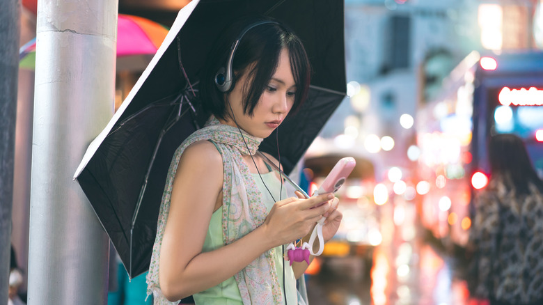 A person wearing Y2K wired over-the-head headphones using an old pink flip phone.